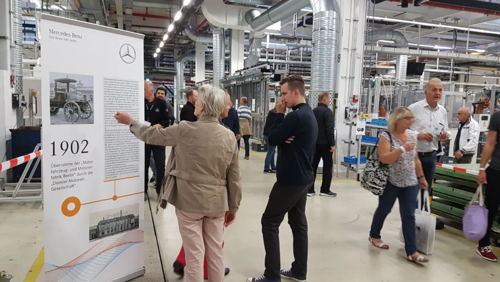 Ein Bild zeigt Personen die den Zeitstrahl der Mercedes Benz AG am Familientag im Werk Berlin betrachten.