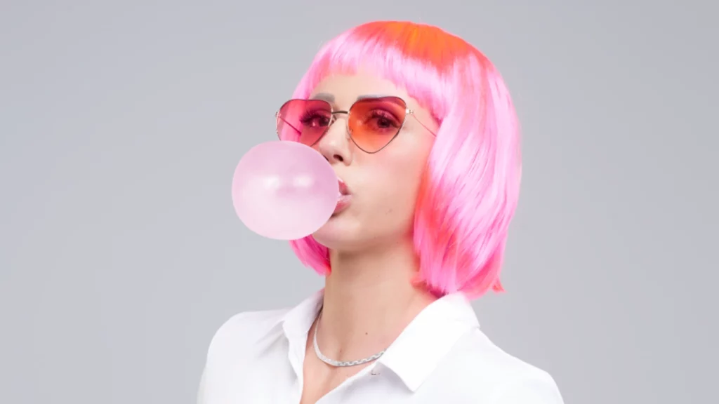 Ein Bild zeigt eine Frau mit Pinken Haaren und Kaugummi aufgepustet für den Dreh der Kampagne "Sexy Toilets, im Blitzlicht" von Wölkchen - der frische Toilette